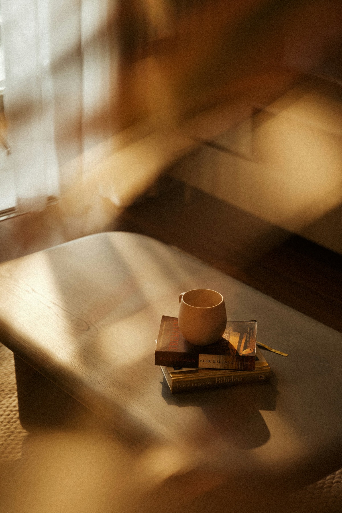 Morning light falling across a wooden bench, with a cup of coffee resting on a small stack of books.